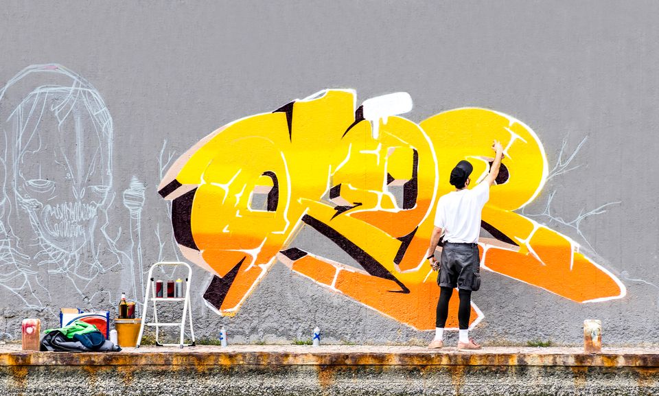 Mand maler farverig grafitti på grå væg